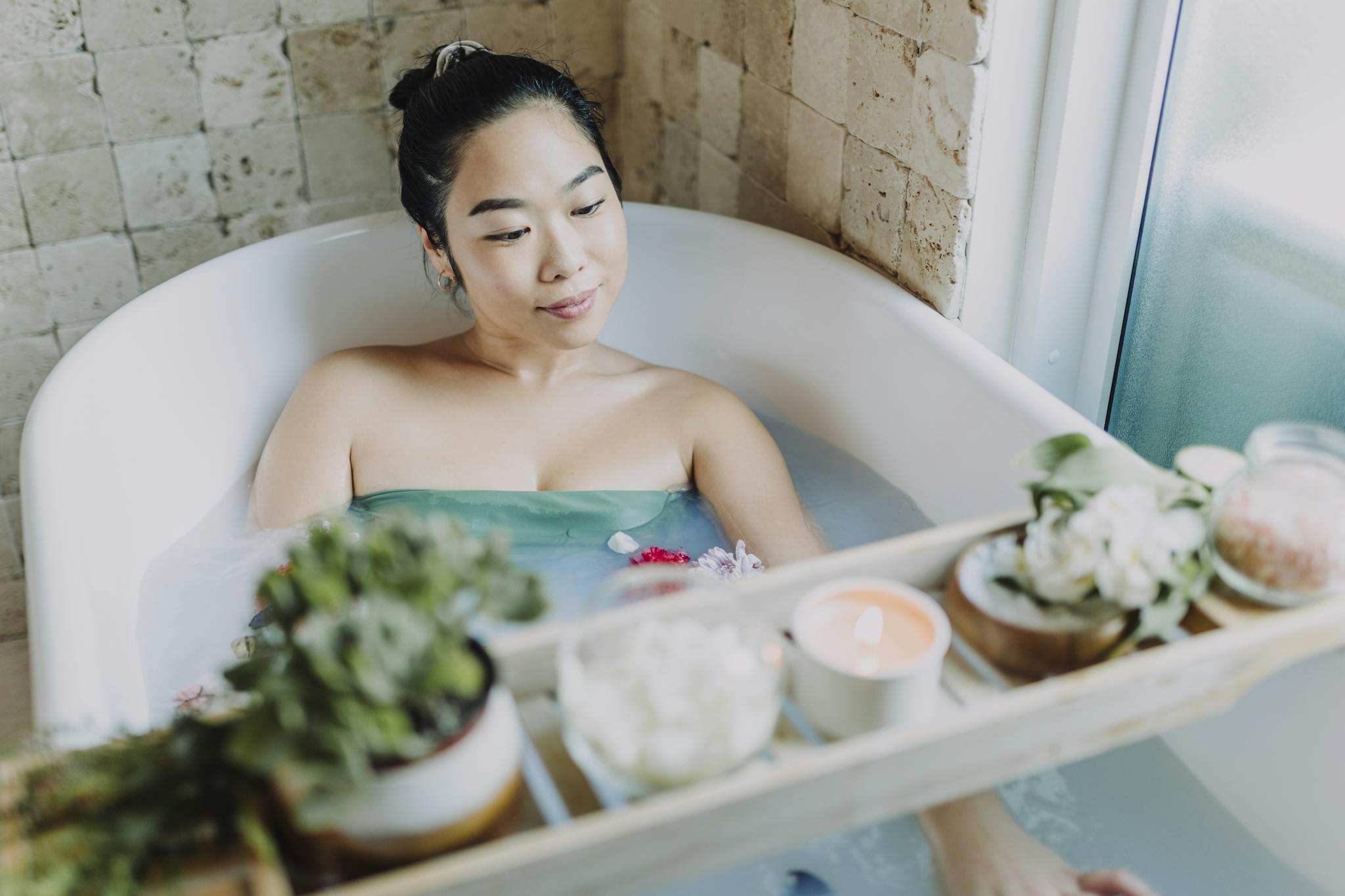 Woman enjoying a soothing bath with candles, flowers, and luxurious spa essentials indoors.