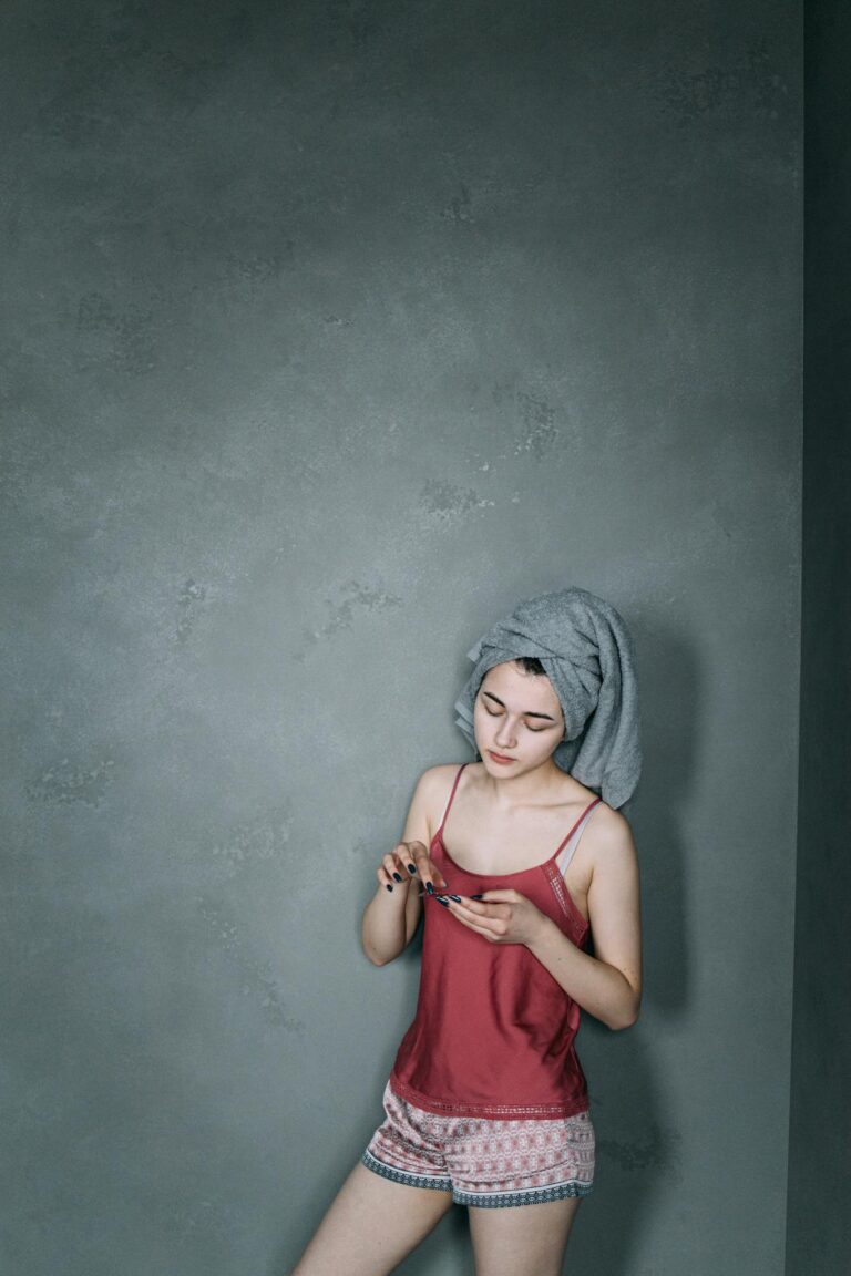 Woman in pajamas with towel on head applying skincare cream in a calm indoor setting.